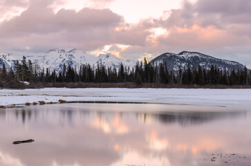 Frozen mountain lake with snow-capped mountains in background at sunset in winter
