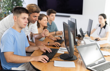 Experienced male instructor assisting motivated young guy mastering computer skills during group...