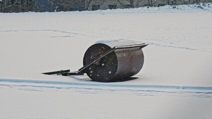 Heavy Metal Lawn Roller Left Outdoor on Sport Field Covered in Snow on Cold Winter Day