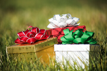 A row of three Christmas presents with colorful wrapping paper and bows, sitting in green grass.