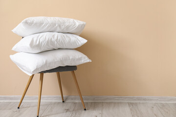 White pillows on chair near beige wall - obrazy, fototapety, plakaty