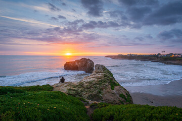 Person sitting on the cliff side of Natural Bridges State Beach in Santa Cruz, CA USA