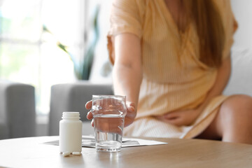 Young pregnant woman taking glass of water and pills on table at home, closeup