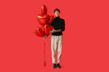 Handsome young man with air balloons in shape of heart on red background. Valentine's Day...