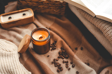 A burning candle with the smell of coffee, an open book and a stack of cozy sweaters, an aesthetic...