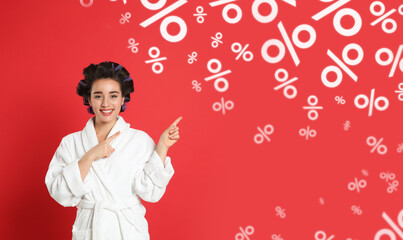 Discount offer. Happy woman in bathrobe with hair curlers pointing at falling percent signs on red...