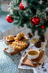 Obraz na płótnie Canvas Cup of hot coffee and bakery goods Various waffles and breads are on the table. and decorated with Christmas There is a Christmas tree and various decorations. to celebrate the Christmas festival.