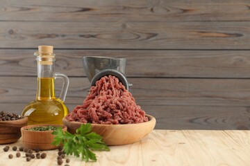 Mincing beef with manual meat grinder. Parsley, oil and spices on wooden table, space for text