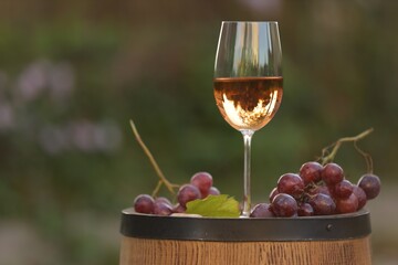Delicious wine and ripe grapes on wooden barrel outdoors, space for text