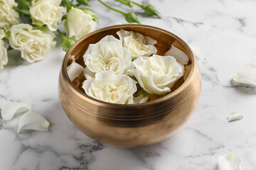 Fototapeta na wymiar Tibetan singing bowl with water and beautiful roses on white marble table, closeup