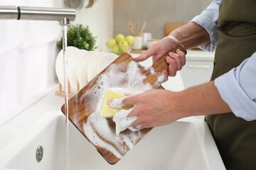 Man washing wooden cutting board in kitchen sink, closeup