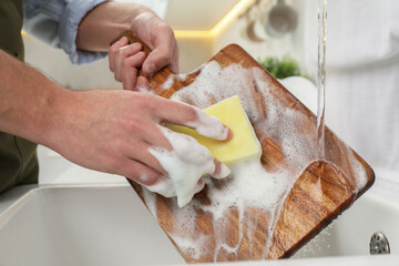 Man washing wooden cutting board in kitchen, closeup