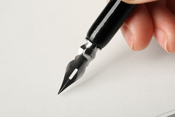 Woman with fountain pen above light paper, closeup