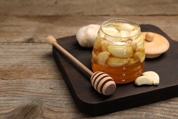 Honey with garlic in glass jar and dipper on wooden table. Space for text
