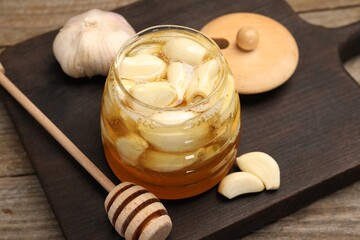 Honey with garlic in glass jar and dipper on wooden table, closeup