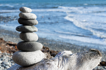 A tranquil image of smooth stacked zen-like stones with blue ocean waves in the background. 