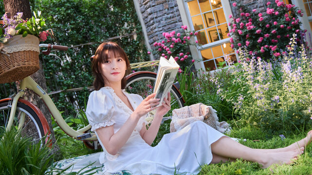 A young beauty sitting on the grass reading a book