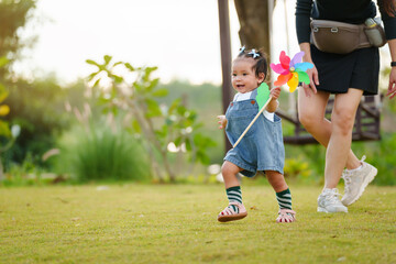 infant baby playing and walking first step on grass field with mother helping in park