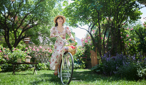 Young and beautiful women ride bicycles in the courtyard full of flowers