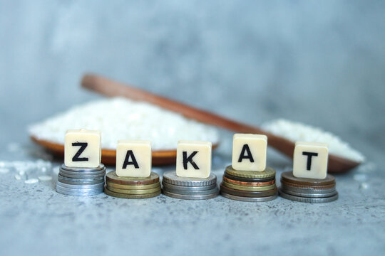 Zakat word on coins stacked with rice grain in the wooden bowl on the background. Islamic zakat fitrah and zakat income concept