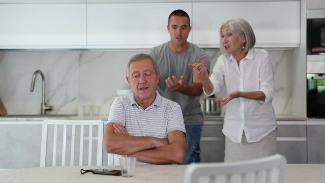 Elderly woman and adult man during family quarrel with elderly man in kitchen