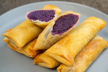 Lumpia ubi ungu is a snack made from purple sweet potato cooked by frying. served on a plate.