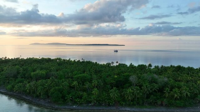 A serene sunrise illuminates the palm-covered, remote island of Koon near Seram, Indonesia. This scenic island's coral reefs, and the surrounding seas, support extraordinary marine biodiversity.