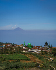 View of the mosque in a small village and the Semeru volcano. There are fields around the village. Sunny day. Batu. East Java. Indonesia.