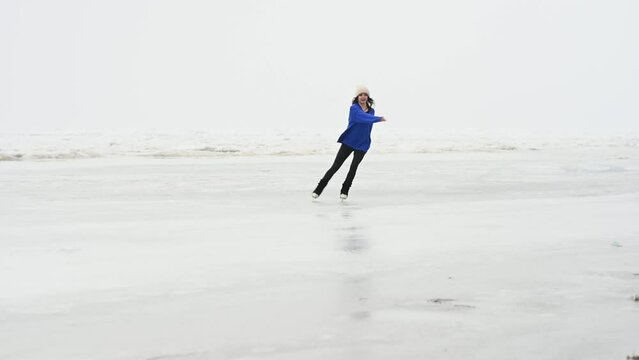 Caucasian woman in a blue sweater is skating on a frozen lake. The figure skater performs the program.