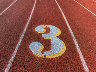 Close up lane number 3 on a new red running track with white lane lines and other markings.