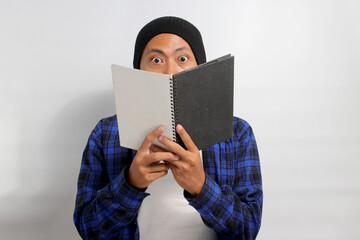 Shocked Asian male student, wearing a beanie and casual clothes and carrying a backpack, is seen...