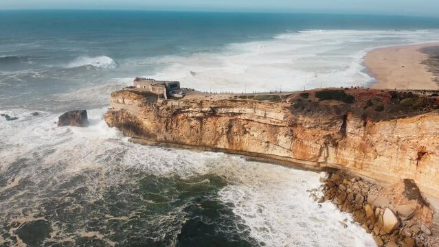 Aerial view of an iconic place on the Atlantic coast, the Mecca of big-wave surfing. View of Nazare lighthouse in Zon North Canyon, place with the biggest waves in Europe, Nazare, Portugal. 4K.