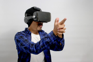 Asian man, wearing VR glasses on his head, imitates a finger pistol gesture while engaged in a Virtual Reality shooter game, aiming and shooting at the target while standing against a white background
