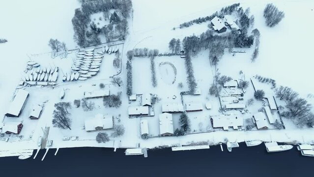 Aerial view northern bank of the village by the river in winter. The whole environment is covered with a thick layer of snow.