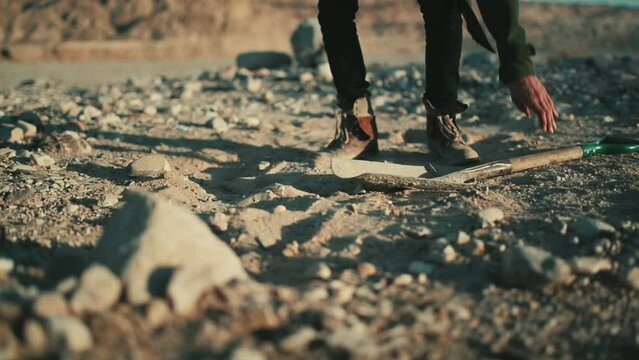 Man picks up spade and starts digging into dry dusty desert soil, low angle