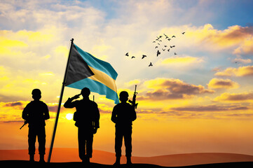 Silhouettes of soldiers with the Bahamas flag stand against the background of a sunset or sunrise....