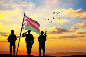 Silhouettes of soldiers with the Belarus flag stand against the background of a sunset or sunrise....