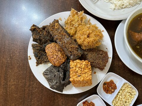 A plate of side dish consists of fried tempeh, cow beef, Potato Perkedel, and Empal in a restaurant