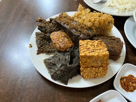 A plate of side dish consists of fried tempeh, cow beef, Potato Perkedel, and Empal in a restaurant