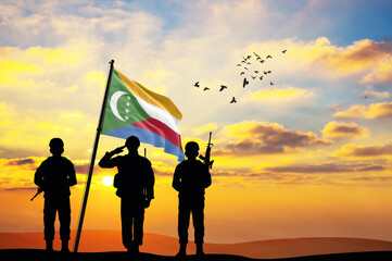 Silhouettes of soldiers with the Comoros flag stand against the background of a sunset or sunrise. Concept of national holidays. Commemoration Day.