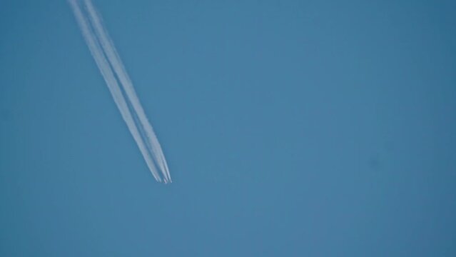 Tilt up shot of a plane cruising the sky leaving a vapor trail behind