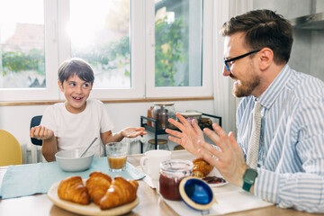 Cheerful boy and his father have fun talking during breakfast at home.