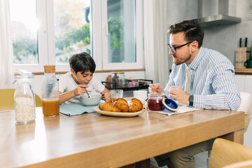 Hungry Caucasian boy eating breakfast with his father.