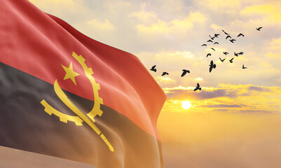 Waving flag of Angola against the background of a sunset or sunrise. Angola flag for Independence Day. The symbol of the state on wavy fabric. - obrazy, fototapety, plakaty