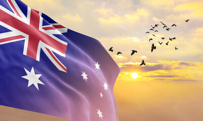 Waving flag of Australia against the background of a sunset or sunrise. Australia flag for Independence Day. The symbol of the state on wavy fabric. - obrazy, fototapety, plakaty