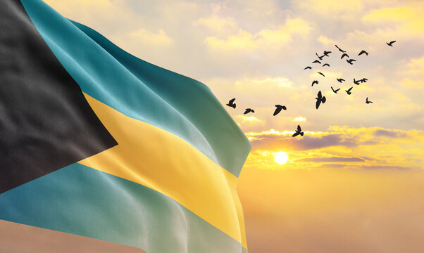 Waving flag of Bahamas against the background of a sunset or sunrise. Bahamas flag for Independence Day. The symbol of the state on wavy fabric. - Powered by Adobe