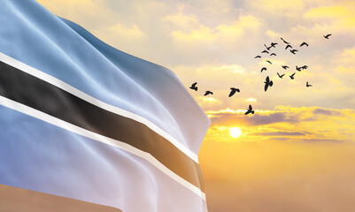 Waving flag of Botswana against the background of a sunset or sunrise. Botswana flag for Independence Day. The symbol of the state on wavy fabric. - obrazy, fototapety, plakaty