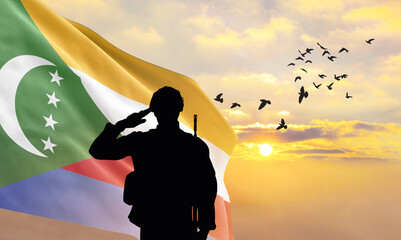 Silhouette of a soldier with the Comoros flag stands against the background of a sunset or sunrise....