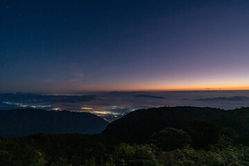 Obraz premium Early morning night sky from the top of Doi Luang Chiang Dao in Chiang Mai, Thailand overlooking a glowing town lights and beautiful dark blue sky