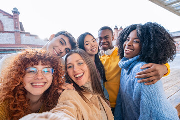 Multi-ethnic young adults smiling for a selfie in bright daylight, showcasing friendship and...